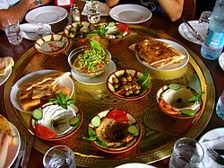 A table with several items, including two plates of flatbreads and assorted dips and salads.