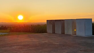 Four concrete blocks stand on a concrete pad, surrounded by undulating grassy land and cornfields.