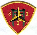A red shield with a gold border. In the center is a pagoda with a black and gold caltrop over it. In the three corners of the shield are the number "3".