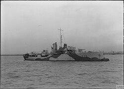 ship at sea steaming from left to right, her guns are unmanned and the bridge crew can be seen