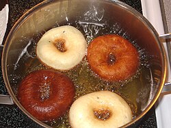 Rings of dough floating in bubbling oil, varying in colour from cream to dark brown
