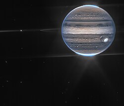 Image of Jupiter showing its faint rings, two small moons, auroras, and atmospheric features.