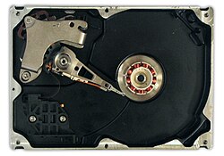 An HDD with disks and motor hub removed, exposing copper-colored stator coils surrounding a bearing in the center of the spindle motor. The orange stripe along the side of the arm is a thin printed-circuit cable, the spindle bearing is in the center and the actuator is in the upper left.